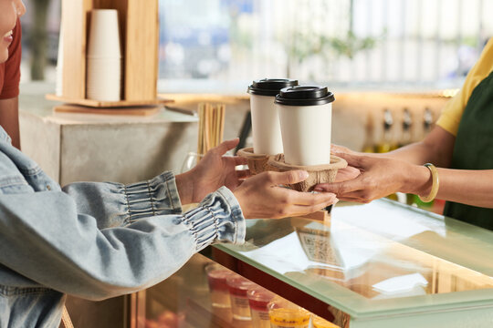 Barista giving take-out coffee holder with two drinks to young couple