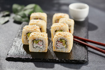 Maki sushi on dark stone table. Sushi roll crab, cheese, cucumber inside and tamago outside. Style concept japanese menu with black background, leaves and hard shadow.