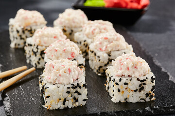 Maki sushi on dark stone table. Sushi roll in seasame and crab topped. Style concept japanesse menu with black background, leaves and hard shadow.