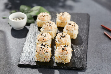 Maki sushi on dark stone table. Sushi roll in seasame and crab topped. Style concept japanesse menu with black background, leaves and hard shadow.