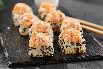 Baked Maki sushi on dark slate. Hot sushi roll with salmon and cheese. Sushi roll sesame outside, baked salmon and cheese topped. Style concept japanese menu with black background