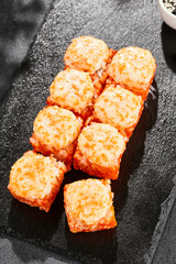 Baked Maki sushi on dark slate. Hot california maki with tobiko. Sushi roll with masago caviar, cheese topped baked oven. Style concept japanese menu with black background, leaves and hard shadow.