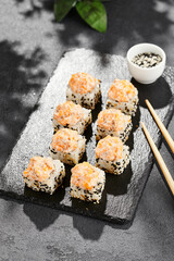 Baked Maki sushi on dark slate. Hot sushi roll with salmon and cheese. Sushi roll sesame outside, baked salmon and cheese topped. Style concept japanese menu with black background