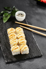 Baked Maki sushi on dark slate. Hot cheese maki with unagi sauce. Sushi roll with baked cheese and unagi sauce topped. Style concept japanese menu with black background, leaves and hard shadow.