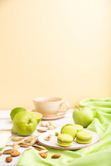 Green macarons or macaroons cakes with cup of coffee on a white and orange background. Side view, selective focus, copy space.