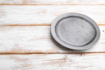 Empty gray ceramic plate on white wooden background. Side view, copy space.
