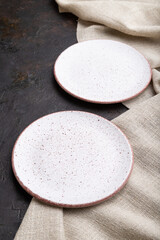 Two empty white plates on black concrete background and linen textile. Side view.