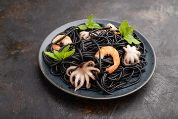 Black cuttlefish ink pasta with shrimps or prawns and small octopuses on black concrete background. Side view.