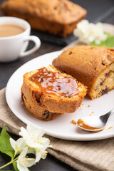 Homemade cake with raisins, almonds, soft caramel and a cup of coffee on a black concrete background. Side view, selective focus.
