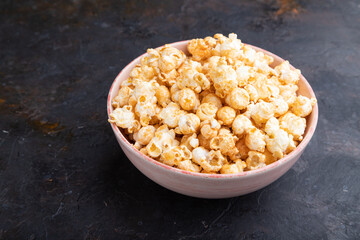 Popcorn with caramel in ceramic bowl on a black concrete background. Side view.