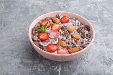 Chocolate cornflakes with milk, strawberry and almonds in ceramic bowl on gray concrete background. Side view.