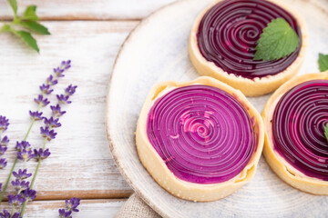 Sweet tartlets with jelly and milk cream with cup of coffee on a white wooden background. Side view, selective focus.