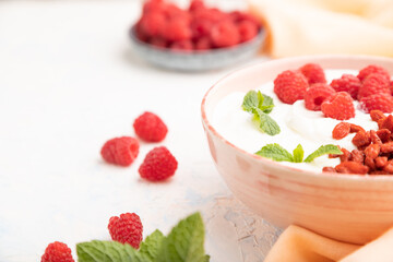 Yogurt with raspberry and goji berries in ceramic bowl on white concrete background. Side view, selective focus.