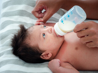 Portrait of Asian mother feeds the Australian Asian three weeks newborn with milk formula from a bottle, concept of motherhood and childhood or infant lying on the white bed.