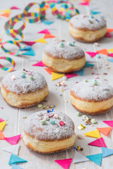 Krapfen, Berliner or donuts with streamers, confetti and mini marshmallows on white wooden background. Colorful vertical carnival or birthday image.