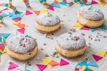 Krapfen, Berliner or donuts with streamers, confetti and mini marshmallows on white wooden background. Colorful carnival or birthday image.