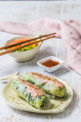 Two summer rolls with salad and salmon and sauce on a white wooden background, japanese, asian food, vertical