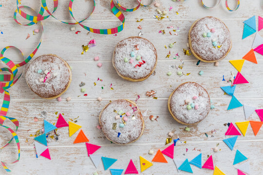 Krapfen, Berliner or donuts with streamers, confetti and mini marshmallows on white wooden background. Colorful carnival or birthday image, top view