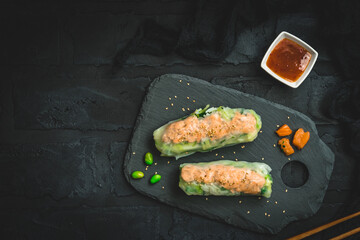 Two summer rolls with salad and salmon on black background, japanese, asian food, top view with copy space