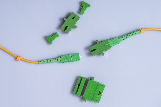 Optical patch cords with SC-APC connector, one patch cord adapter inserted, single and double SC-APC adapters lie nearby, light background