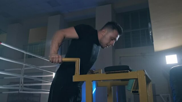 Young man doing triceps dips on parallel bars at dark gym. Side view of sporty male training indoors. Man bars workout. 4k, UHD. Medium shot