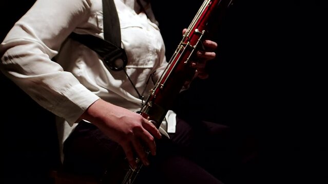 Female musician plays jazz on bassoon tune in studio on dark background, side view. Woman plays bassoon with fingers in keys