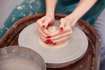 women's hands with a beautiful red manicure work on a potter's wheel, sculpt a bowl of dirty raw clay.