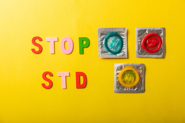 Colorful blocks with "STOP STD" phrase background, flat lay. Super safe strawberry condoms with a pleasant smell on a yellow background. Contraceptives are made from natural rubber latex, high