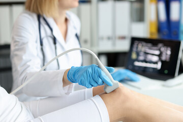 Doctor doing ultrasound examination of patient knee joint in clinic closeup