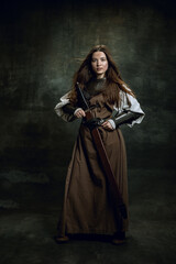 Full-length portrait of seriuos beautiful woman in image of medieval warrior or knight with dirty...