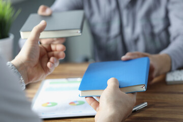 Businesspeople exchange notebooks in office, men give to each other books