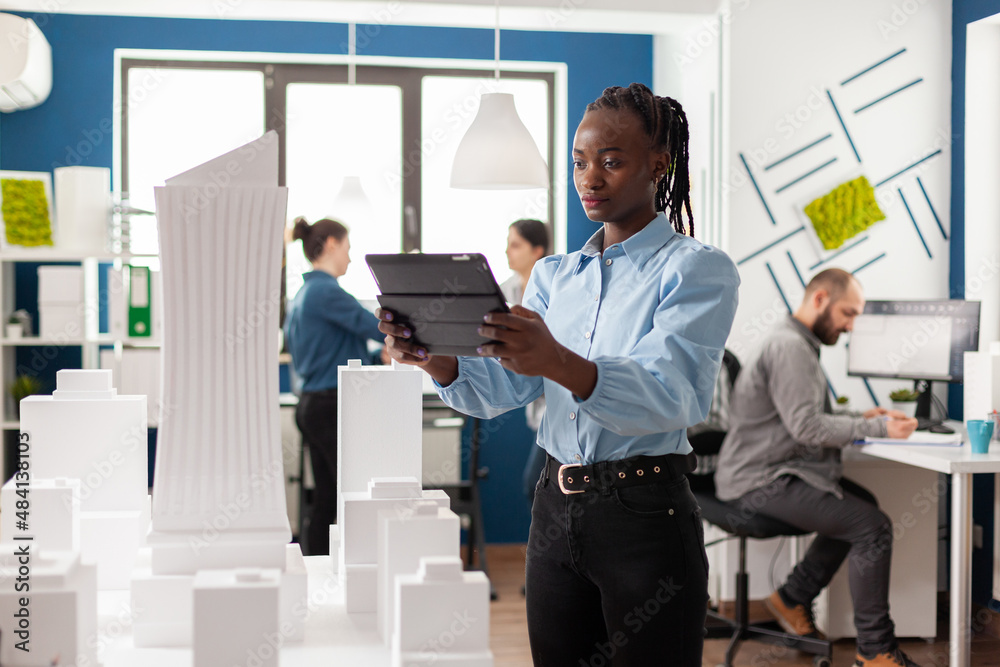Poster architect looking at tablet in front of white foam building model in architectural office. engineer 