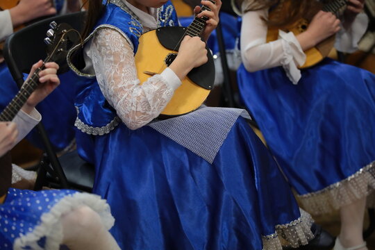 A woman playing a stringed musical instrument domra in folk traditional clothes performing in an orchestra at a concert