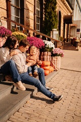 Fototapeta premium a happy family with a small child on steps decorated with autumn flowers. 