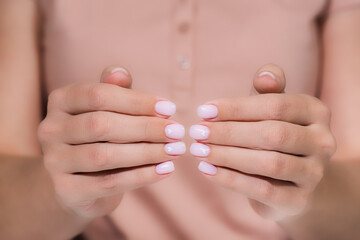 Closeup top view of elegant pastel pink natural manicure. Horizontal color photography of manicured female hands with holiday Valentines day or wedding nail design. Pink nails with white hearts