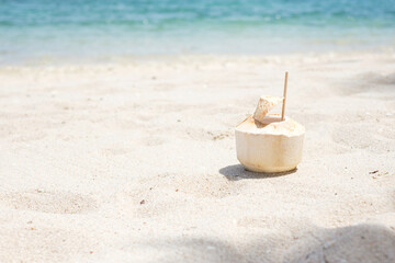 Fototapeta na wymiar Fresh coconut juice and straw on white sand against tropical beach background. Summer, relaxing and vacation concepts