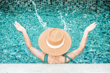 Happy woman in green swimsuit and hat in swimming pool at luxury hotel against ocean front. young female enjoy in tropical resort. Relaxing, summer,  travel, holiday, vacation and weekend concept