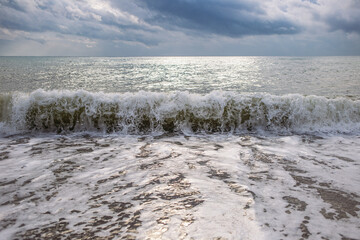 Stock photography of beautiful cloudy stormy sunny sea landscape with big splashing on beach foamy sea waves