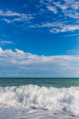 Fototapeta na wymiar Vertical color photography of beautiful sunny sea beach with splashing foamy waves and clear blue sky