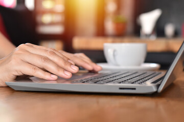 Close-up view, Woman hand typing on laptop with blurred white coffee cup.