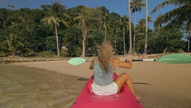 Sportive woman rows pink plastic canoe along sea water
