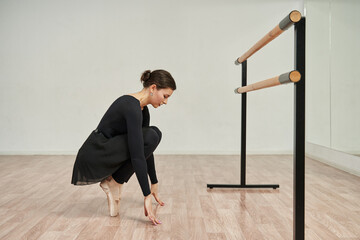 a young ballerina stands in pointe shoes on her toes, gracefully keeps his hands on the floor in front of him. in front of a ballet barre, in front of a mirror