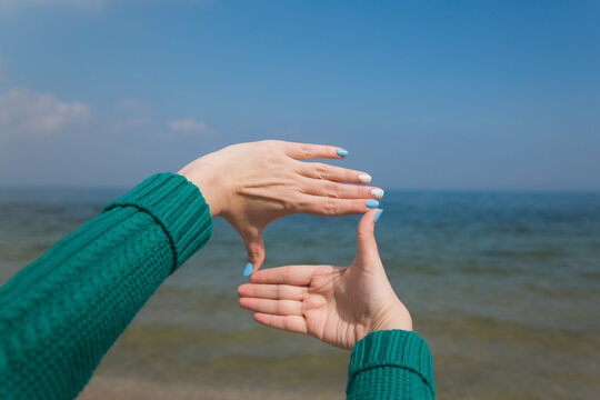 Close-up point of view shot photography of female caucasian hands isolated on blue sky background. Young woman forming frame with her two hands as if looking at something virtual and invisible