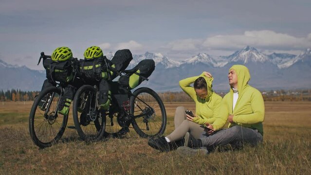 The man and woman travel on mixed terrain cycle touring with bikepacking. The two people journey with bicycle bags. Mountain snow capped.