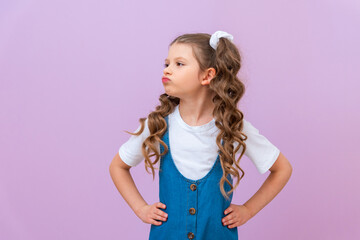 The upset child keeps his hands on his waist and puffed out his cheeks. A little girl with a bad mood on an isolated background.
