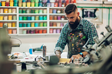 Male worker pressing ink on frame while using the printing machine in a workshop