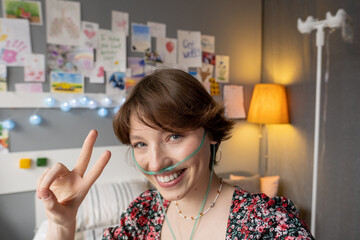 Close-up of happy sick girl with oxygen tube in her nose smiling at camera sitting at hospital ward