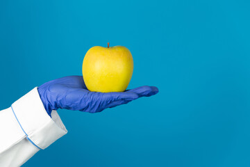 Doctors hand in a glove holds an apple on a blue background with copy space