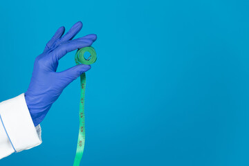 Doctors hand in a glove holds a measuring tape on a blue background with copy space