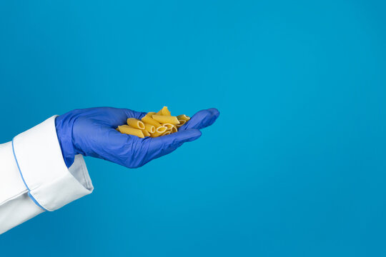 Doctors hand in a glove holds a macaroni pasta on a blue background with copy space